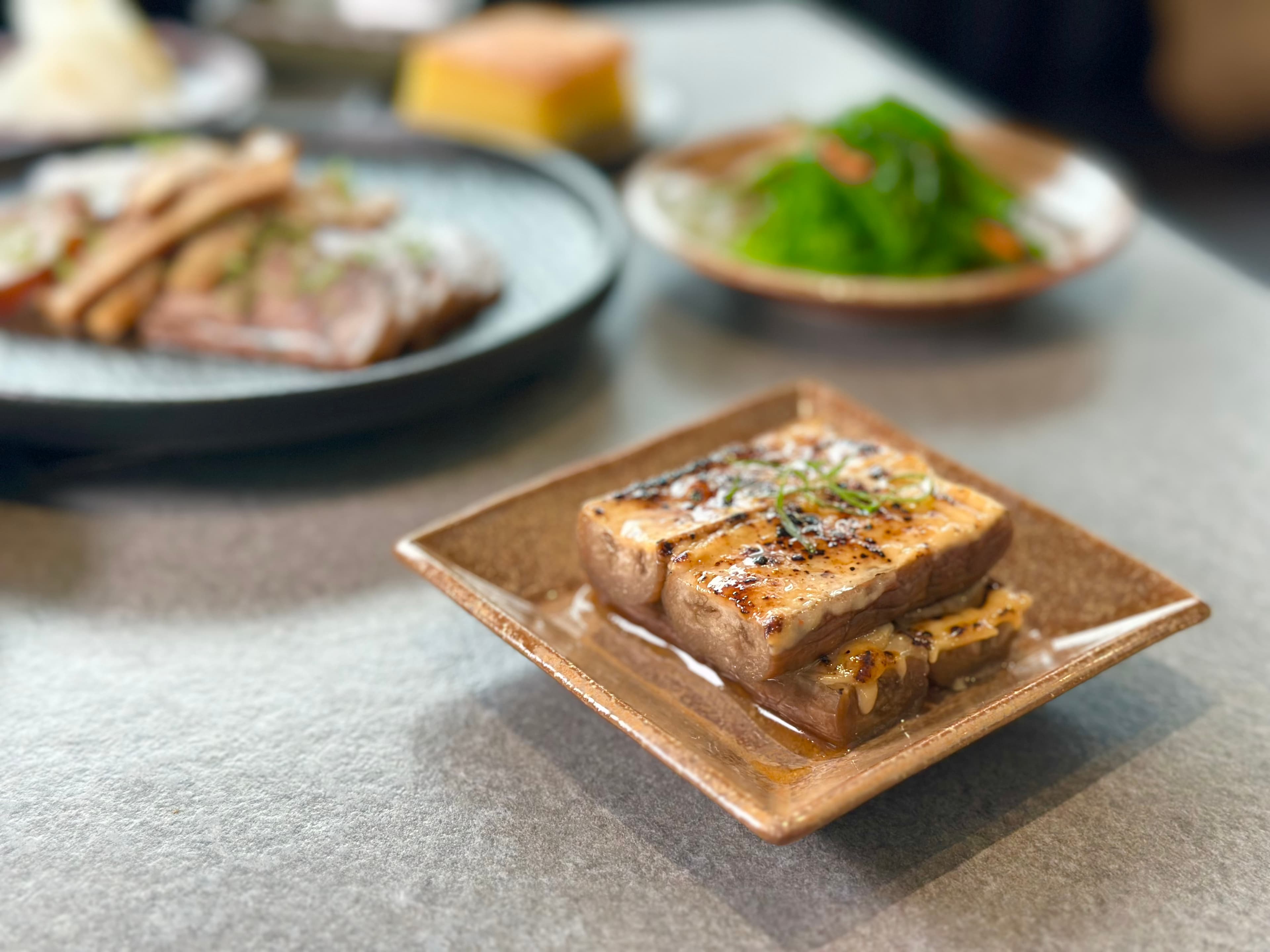 「烤茄子」口感軟嫩，帶著白味噌與是拉差辣椒醬的甜辣。（80元／份）